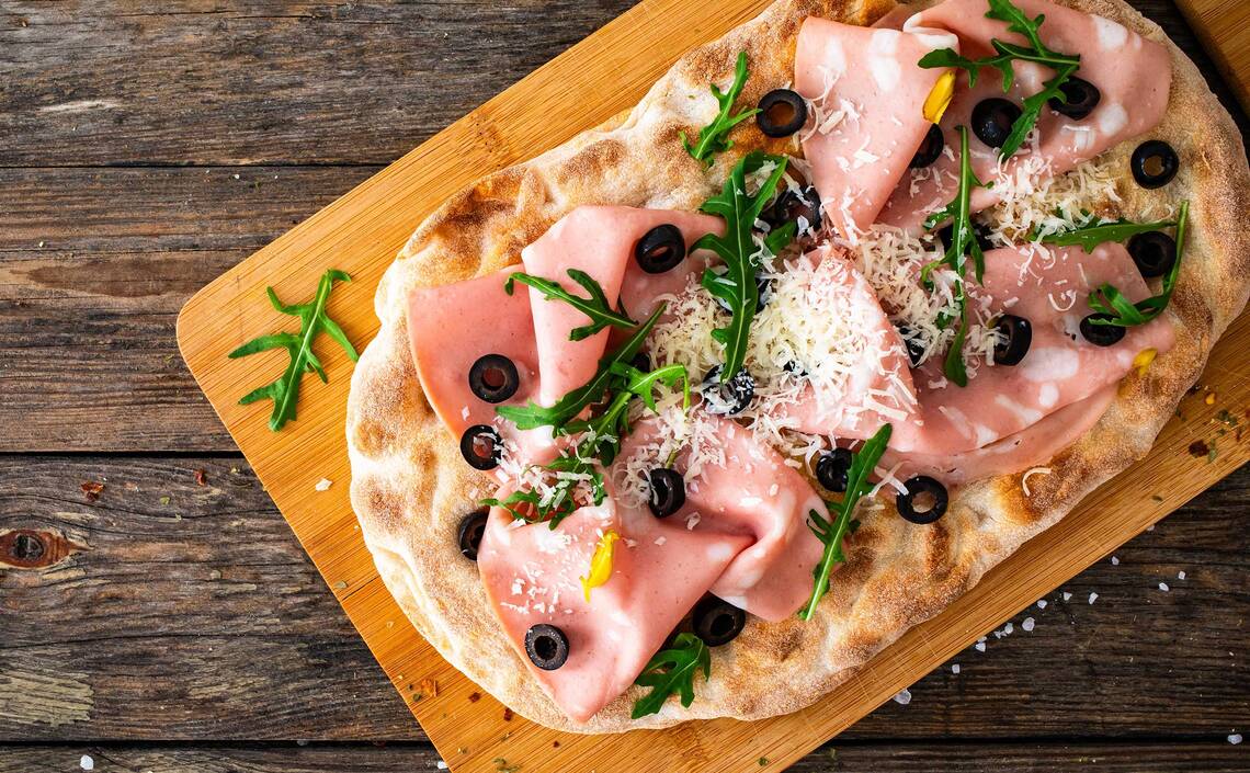 Pinsa mit Schinken, Oliven, Rucola und Parmesan 