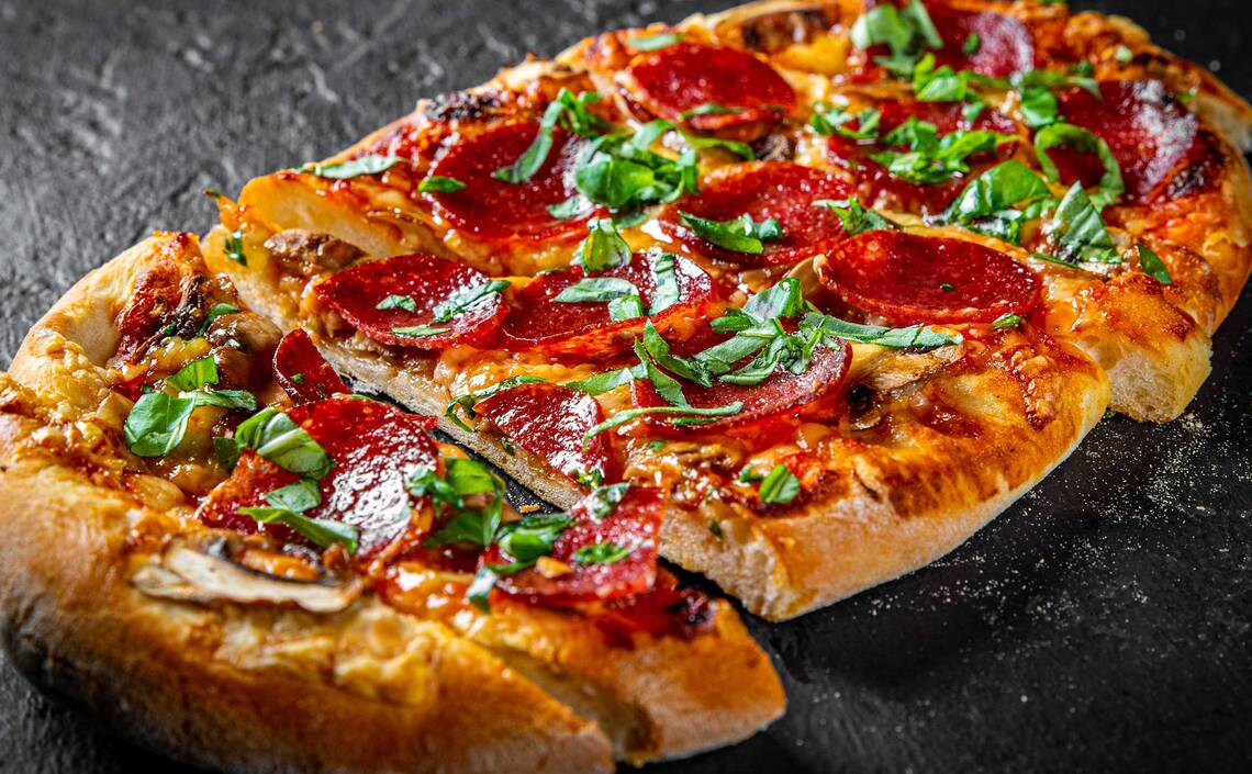 Geschnittene Pinsa mit Tomatensauce, Käse, Salami und Basilikum 